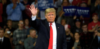 A man in a suit waving to a cheering crowd at a political rally