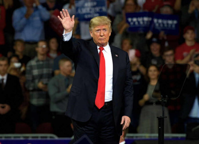 A man in a suit waving to a cheering crowd at a political rally