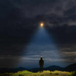 A mysterious figure standing on a mountain under a dark sky with a beam of light from a UFO
