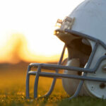 Close-up of a football helmet on a grassy field during sunset