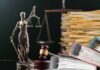 A bronze statue of Lady Justice holding scales, with legal documents and a gavel in the background