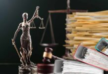 A bronze statue of Lady Justice holding scales, with legal documents and a gavel in the background