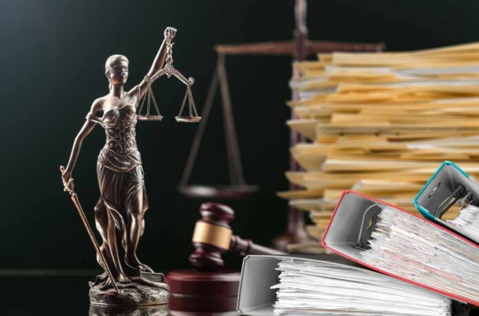 shutterstock_2274157631.jpg A bronze statue of Lady Justice holding scales, with legal documents and a gavel in the background