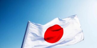 Japanese flag with a red circle on a white background waving against a blue sky