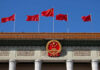 Chinese flags and national emblem displayed on a government building against a blue sky