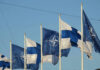 Flags of Finland and NATO waving in the wind against a clear blue sky