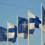 Flags of Finland and NATO waving in the wind against a clear blue sky