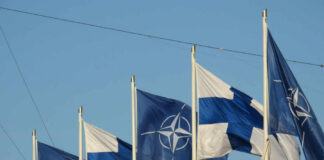 Flags of Finland and NATO waving in the wind against a clear blue sky