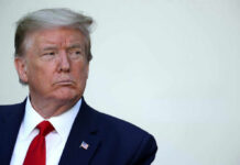 A serious-looking man in formal attire with an American flag pin