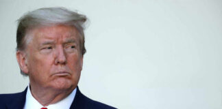 A serious-looking man in formal attire with an American flag pin