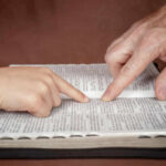A childs hand and an adults hand pointing at text in a book
