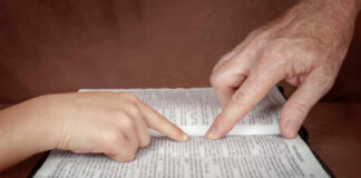 A childs hand and an adults hand pointing at text in a book