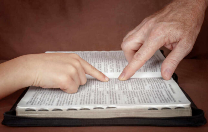 shutterstock_1075033505.jpg A childs hand and an adults hand pointing at text in a book