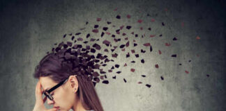 A woman with glasses holding her head, with fragments dispersing from her head