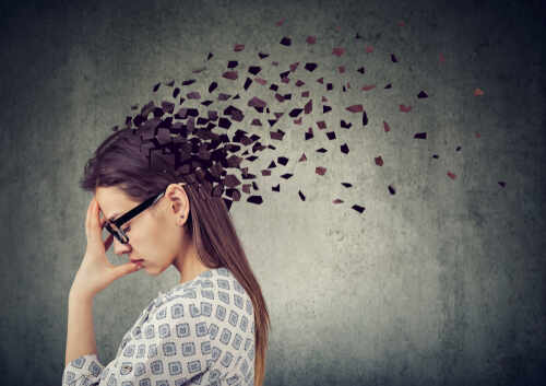 shutterstock_1112176976 (1).jpg A woman with glasses holding her head, with fragments dispersing from her head