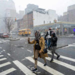 People crossing a snowy street in an urban area during a winter storm