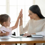 A mother and daughter sharing a high-five while studying together