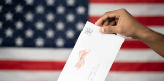 A hand placing a ballot into a voting box with an American flag background