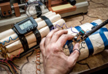 A hand working on a device resembling an explosive with wires and a timer