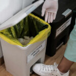 Person in gloves disposing of waste in an infectious waste bin