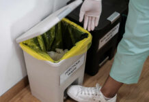 Person in gloves disposing of waste in an infectious waste bin