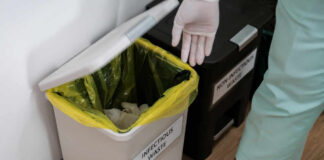 Person in gloves disposing of waste in an infectious waste bin