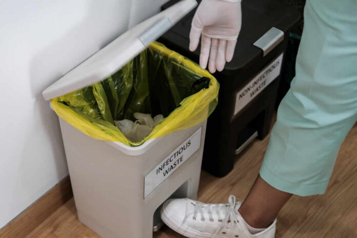 Person in gloves disposing of waste in an infectious waste bin