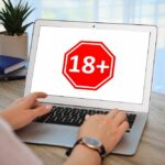 Person using a laptop displaying an age restriction sign
