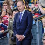 A man in a suit stands among a crowd at a public event