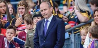 A man in a suit stands among a crowd at a public event