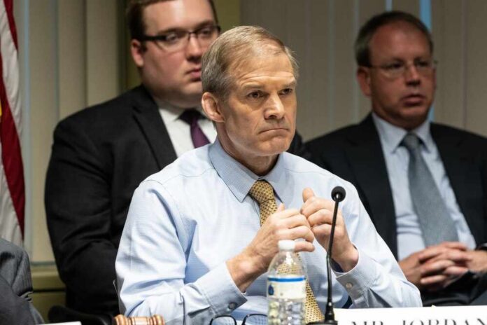 A serious-looking man in a formal shirt and tie sitting at a panel during a government hearing