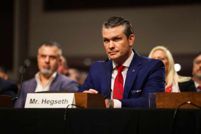 A man in a blue suit and red tie sitting at a hearing table with a nameplate