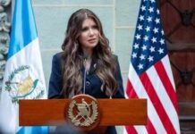 A government official delivering a speech at a podium with flags in the background