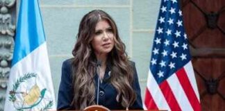 A government official delivering a speech at a podium with flags in the background