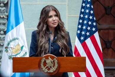 A government official delivering a speech at a podium with flags in the background