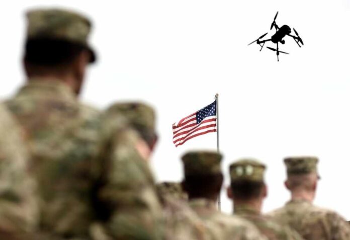 Military personnel standing in formation with a drone flying overhead and an American flag in the background