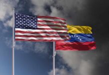 Flags of the United States and Venezuela waving against a cloudy sky