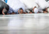 Group of men in traditional attire performing prayer on the floor