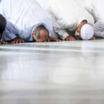Group of men in traditional attire performing prayer on the floor