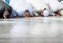 Group of men in traditional attire performing prayer on the floor
