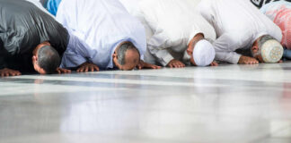 Group of men in traditional attire performing prayer on the floor