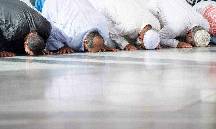 Group of men in traditional attire performing prayer on the floor