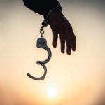Silhouette of a hand holding handcuffs against a sunset