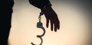 Silhouette of a hand holding handcuffs against a sunset