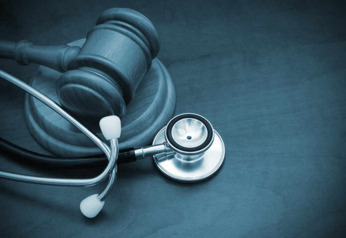 shutterstock_1358884013.jpg A wooden gavel next to a stethoscope on a dark surface