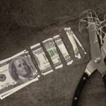 Scissors cutting through shredded dollar bills on a dark surface