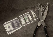 Scissors cutting through shredded dollar bills on a dark surface