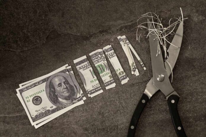 Scissors cutting through shredded dollar bills on a dark surface