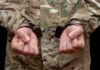 Person in military uniform with hands cuffed together