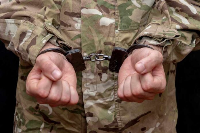 Person in military uniform with hands cuffed together